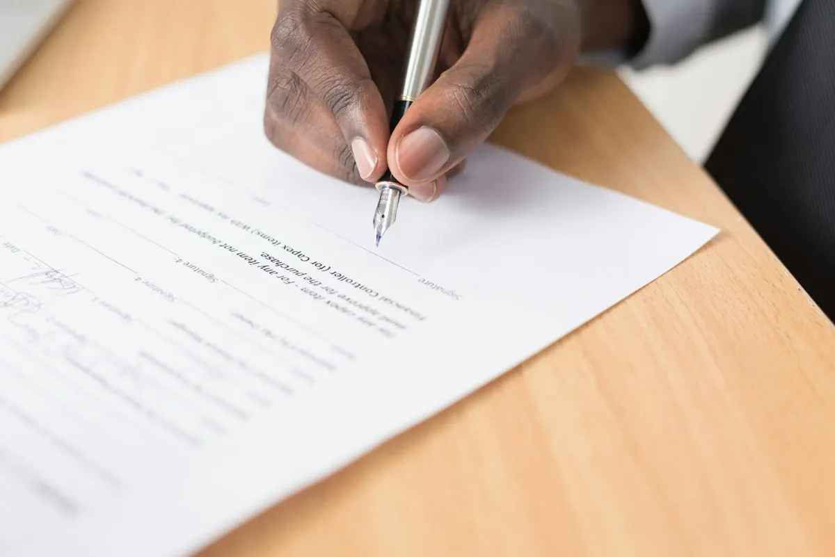 A hand signing a contract page with a fountain pen, the cloud contract the Bank of Tanzania approves before implementation