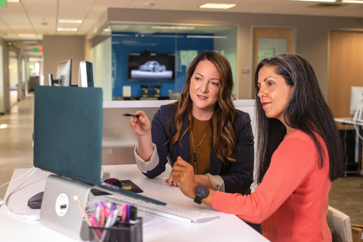 Two people at an office table looking at the same laptop screen during a supplier meeting