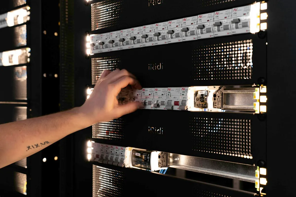 A hand on a row of rack-mounted circuit breakers: a MongoDB Atlas migration cutover is one switch, thrown after the checks pass